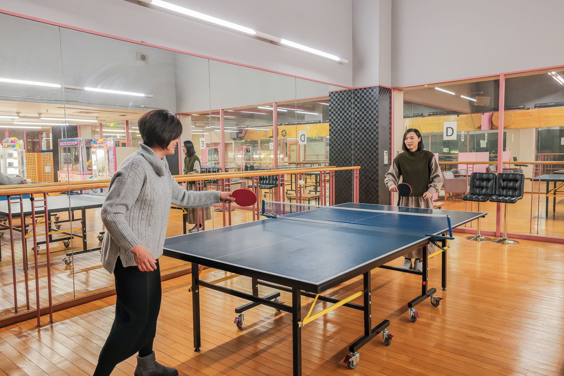 Une table de ping-pong dans une pièce dont le sol est en bois et qui est séparée par des cloisons en verre.