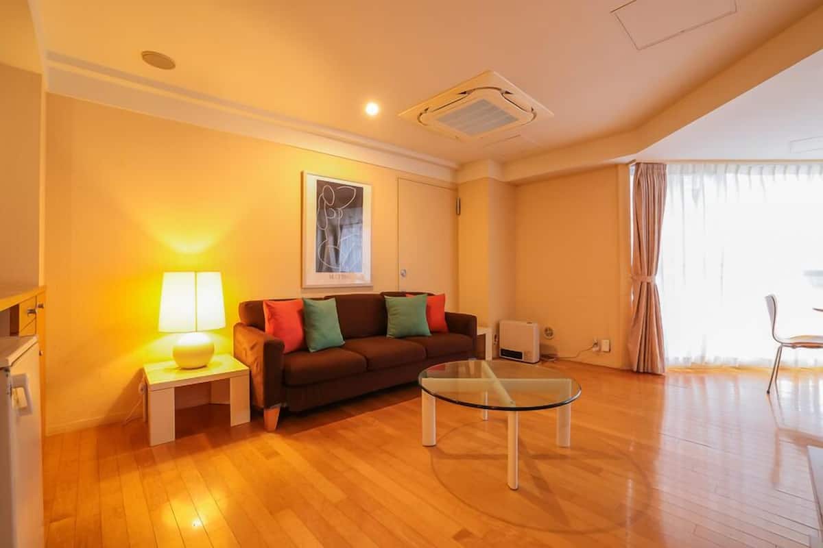 Ein Wohnzimmer mit einer Couch, einem Glastisch, einer Lampe, einem Bild an der Wand und einem Fenster mit Vorhängen.