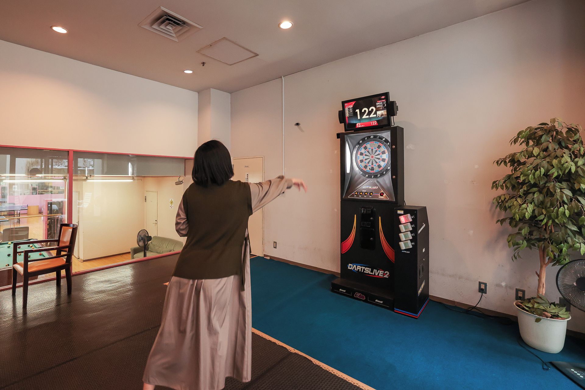 A person playing darts in a room with a dartboard and a dart machine.