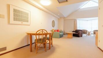 A spacious living area with a dining table, chairs, a sofa, and a large window providing natural light.