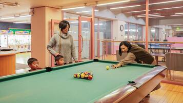 A pool table in a room with a wooden floor, a glass partition, and a clock on the wall.