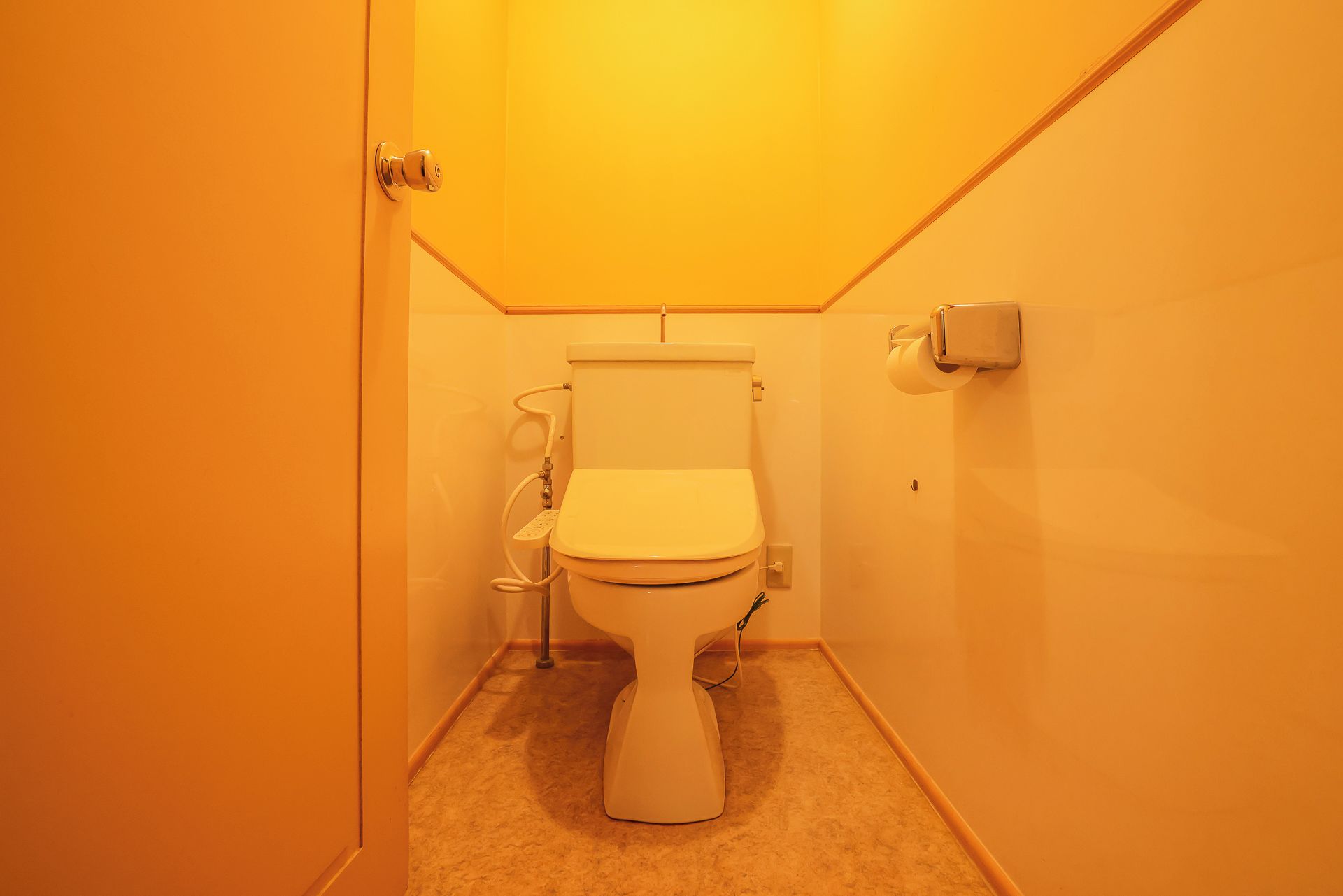 Un baño pequeño y estrecho con inodoro, secamanos y dispensador de toallas de papel.