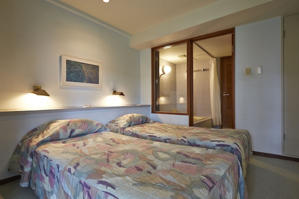 A bedroom with two beds, a bathroom with a shower, and a door leading to another room.