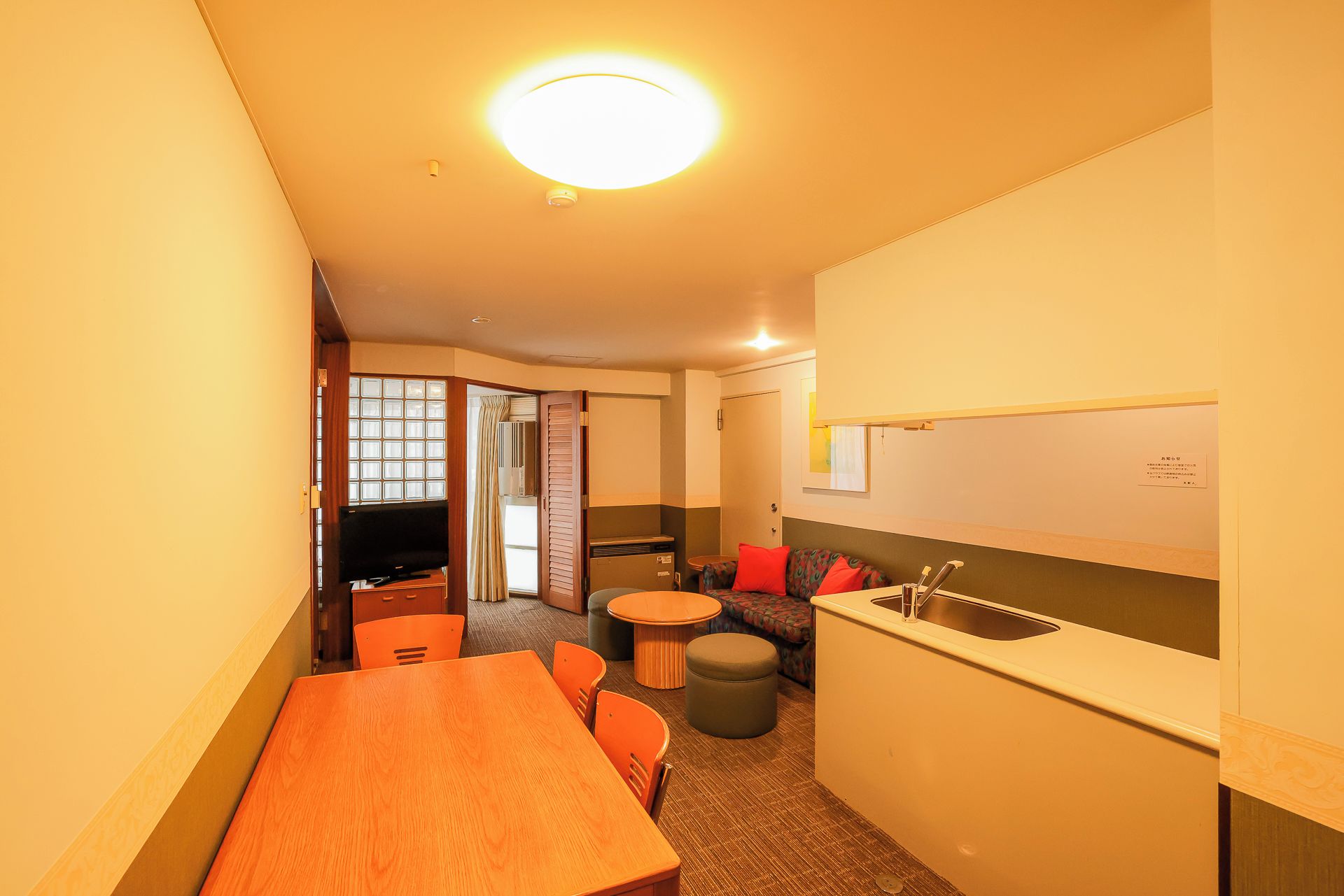 A compact hotel room with a kitchenette, a dining area, and a television.