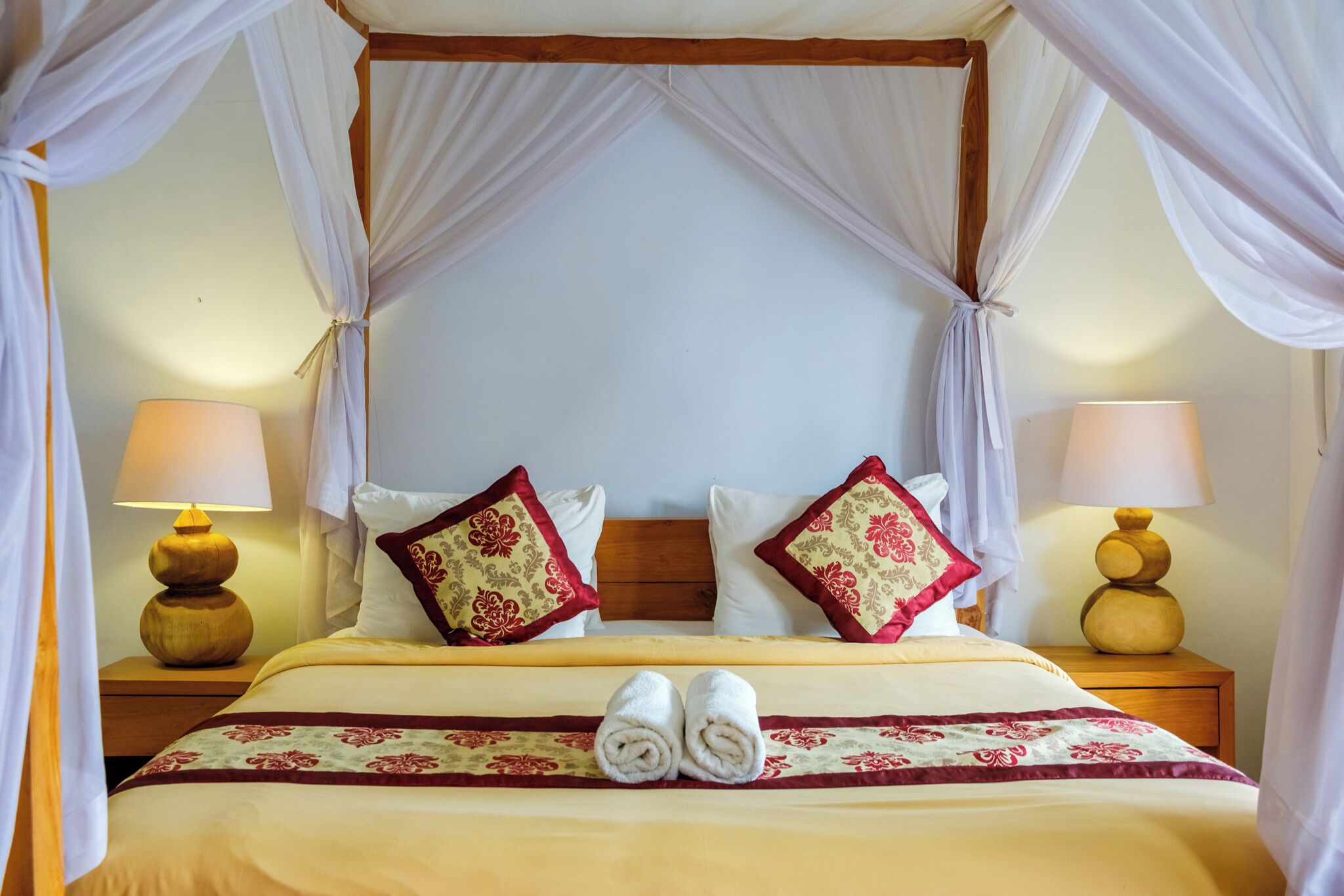 A four-poster canopy bed with two pillows, a bedspread with a floral pattern, and two bedside lamps.