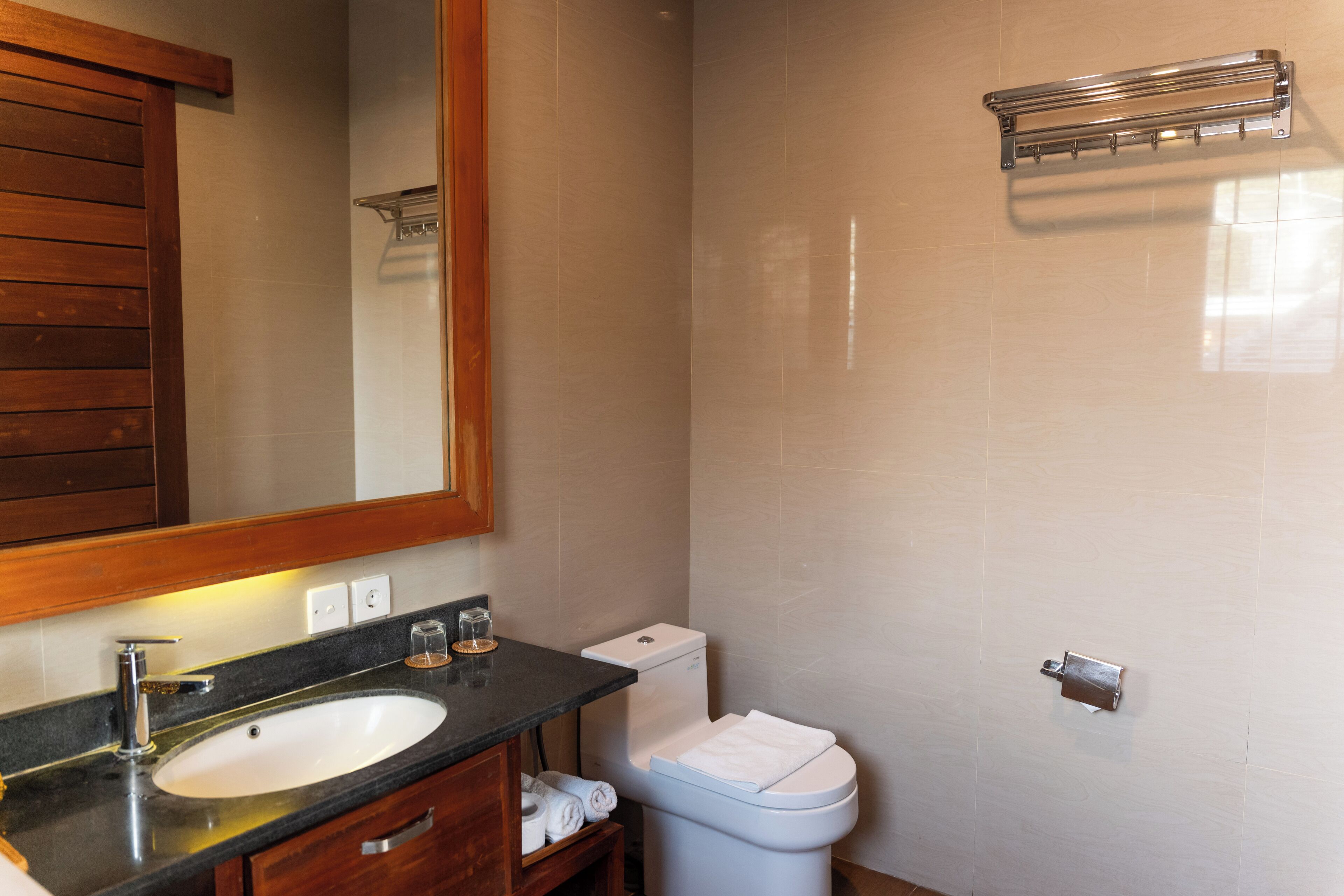 A bathroom with a wooden vanity, a sink, a mirror, a toilet, and a towel rack.
