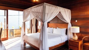 A wooden four-poster bed with a canopy, a bedside table with a lamp, and a view of the outdoors through a glass door. - Lebak Bali Residence (Canggu)