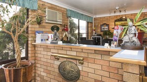 A reception desk with a brick wall, a potted plant, a brass plaque, and a statue. - Ningana Motel (Mudgee)