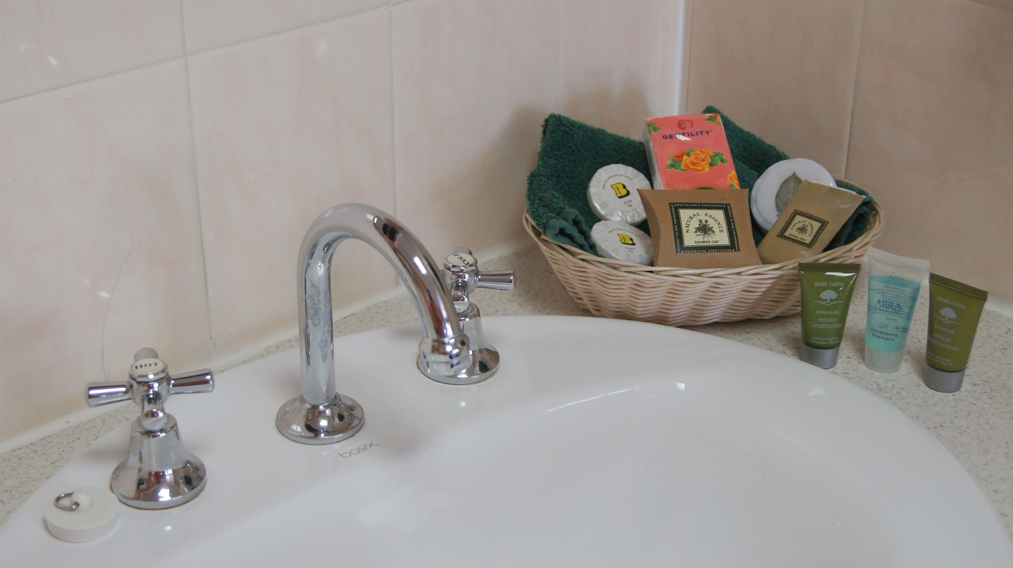 A bathroom sink with a chrome faucet, a basket of toiletries, and three bottles of skincare products.