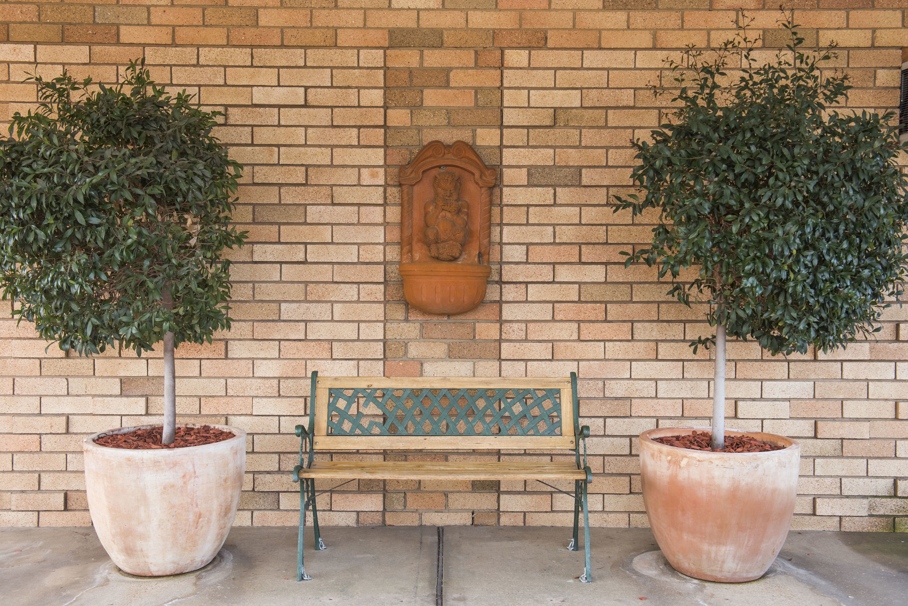 A bench with a decorative backrest in front of a brick wall with a relief sculpture.