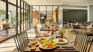 A spacious dining area with large windows, multiple tables, and a variety of dishes. - The Wind (Sattahip)