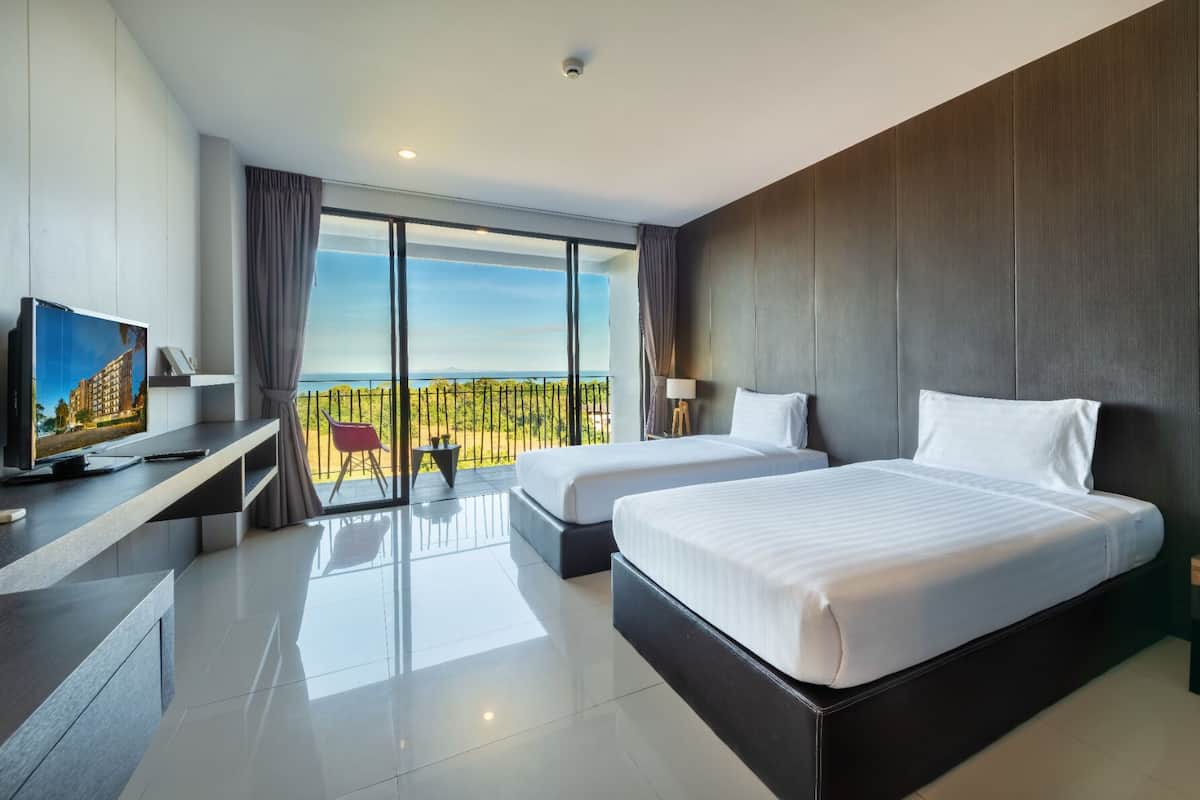 A modern hotel room with two beds, a TV, a desk, and a balcony with a view.