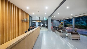 A modern reception area with a wooden slat wall, a reception desk, and a seating area with outdoor furniture. - The Wind (Sattahip)