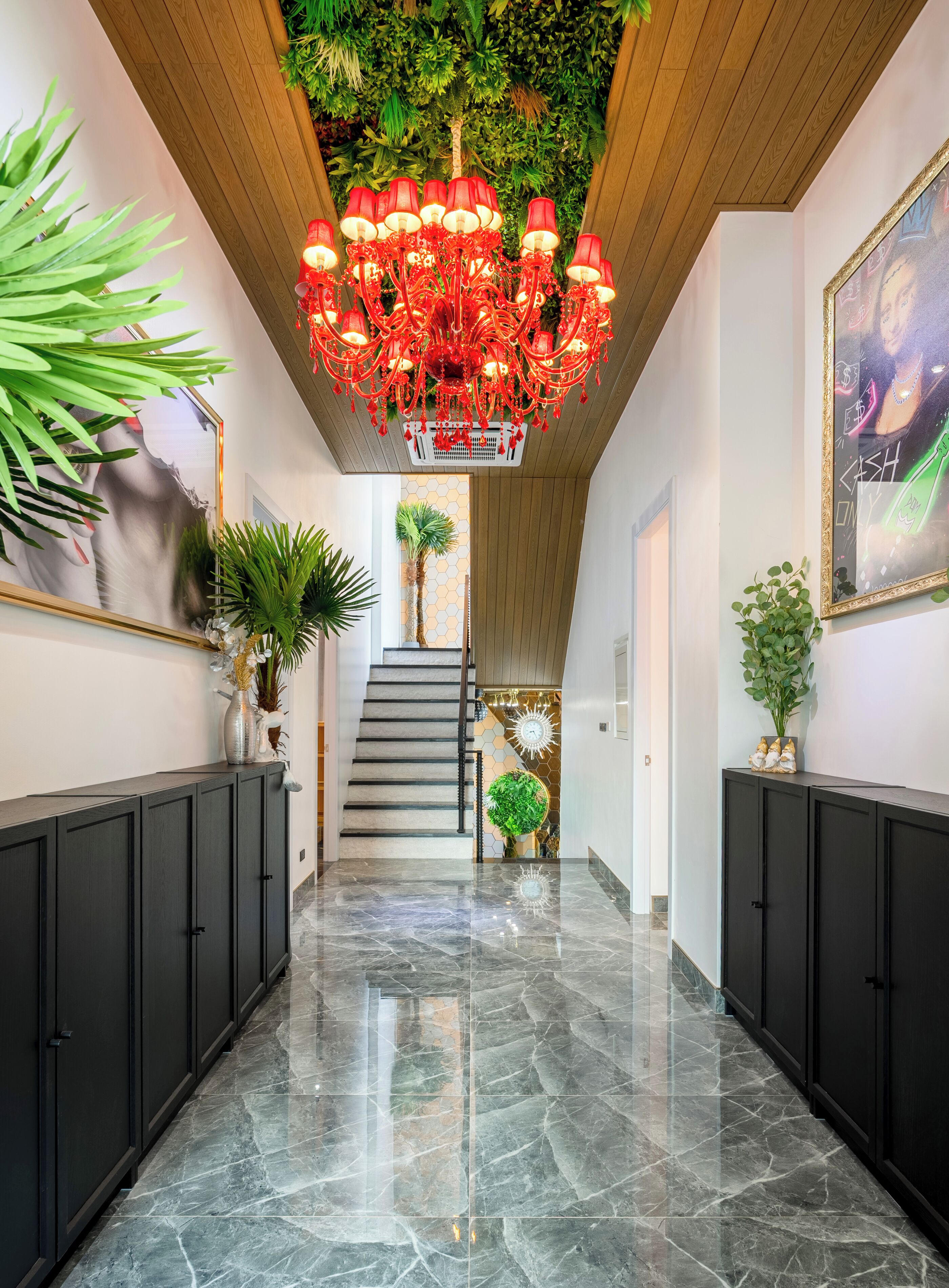 A hallway with a marble floor, black cabinets, a staircase, and a red chandelier.