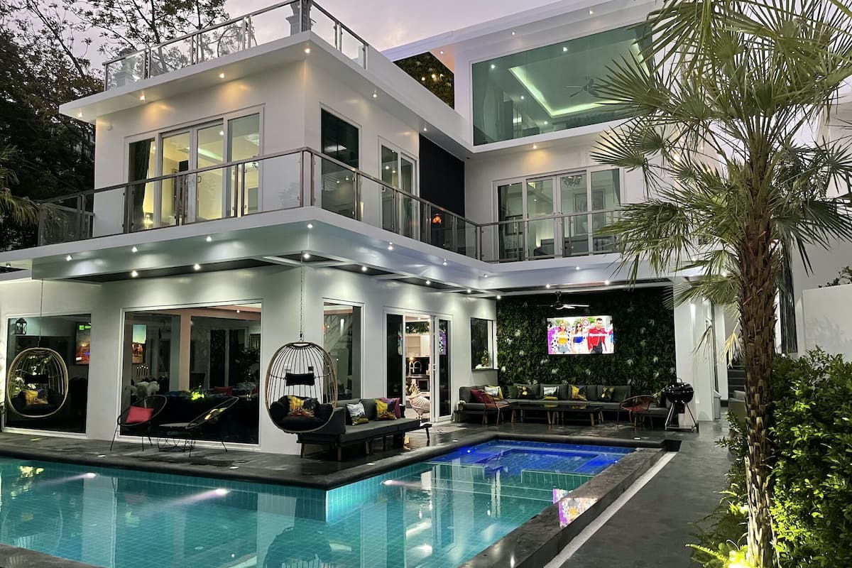 A modern two-story house with a swimming pool, large windows, and a flat roof.