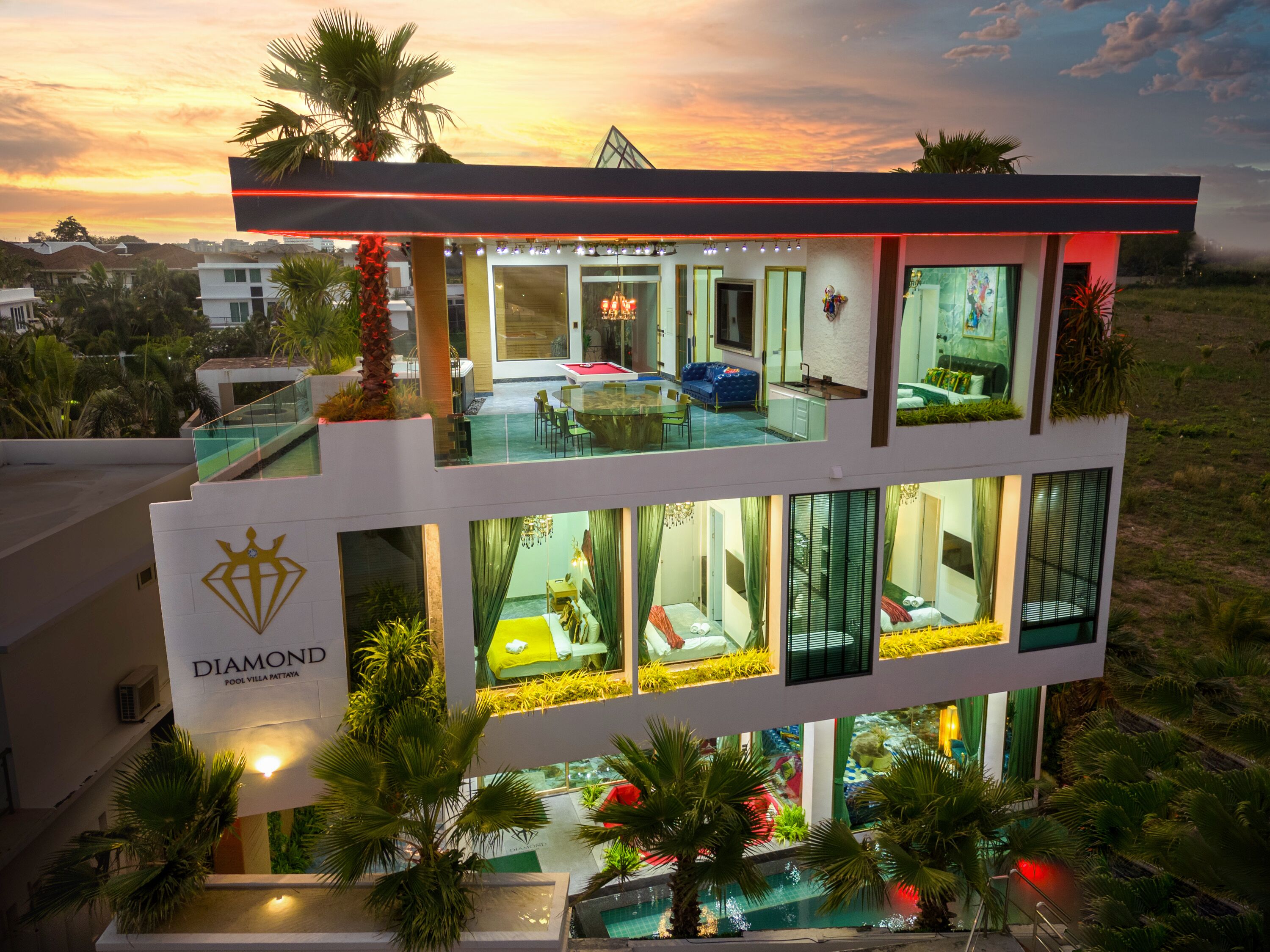 A multi-story hotel with a pool on the ground floor, a dining area on the upper floor, and a view of the sunset.