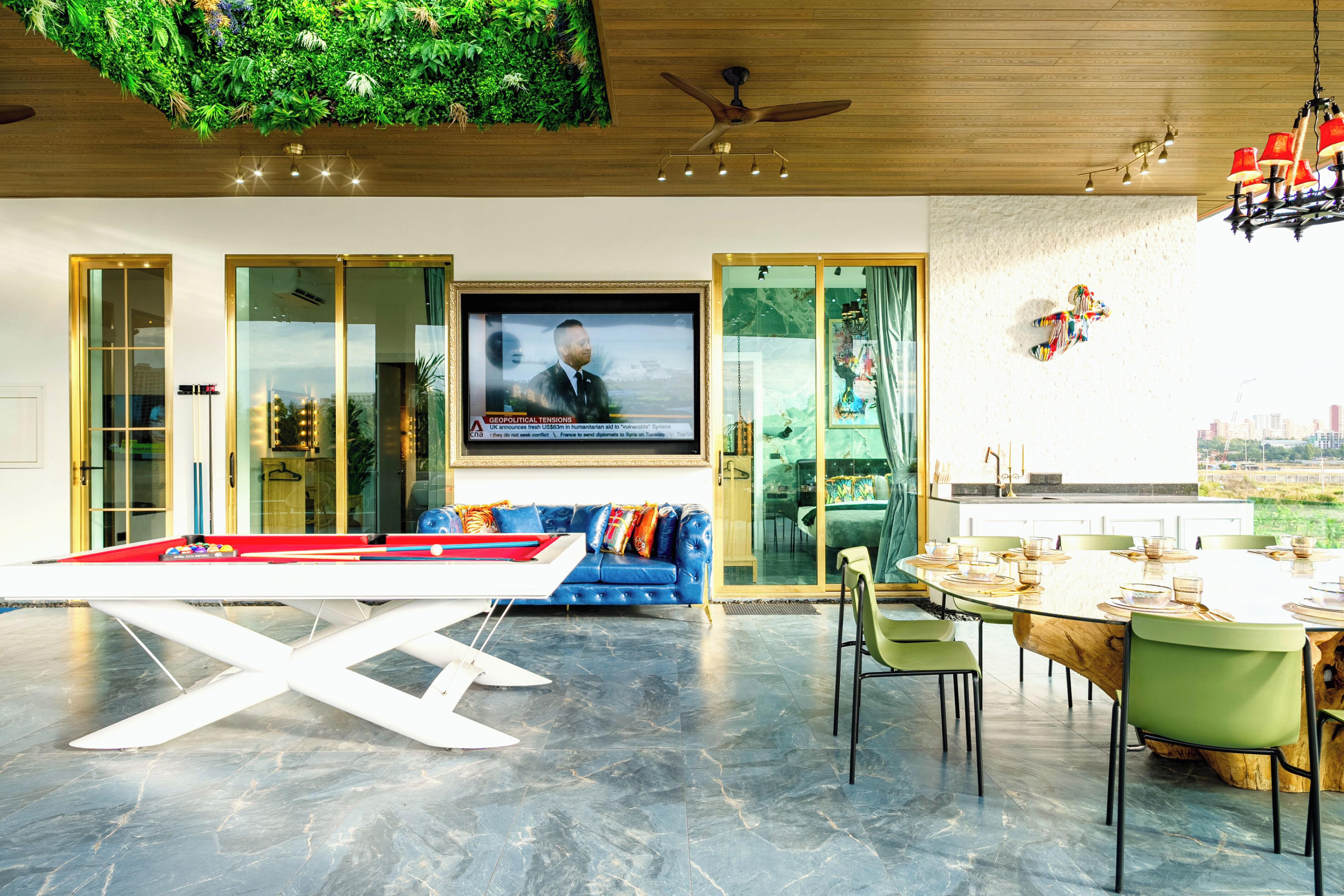 A modern living room with a pool table, a blue sofa, and a dining area with green chairs.