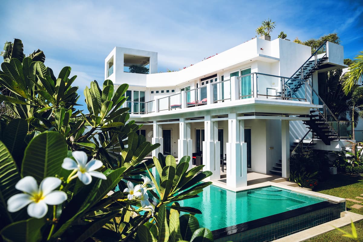 A modern two-story building with a pool, surrounded by lush greenery and tropical plants.