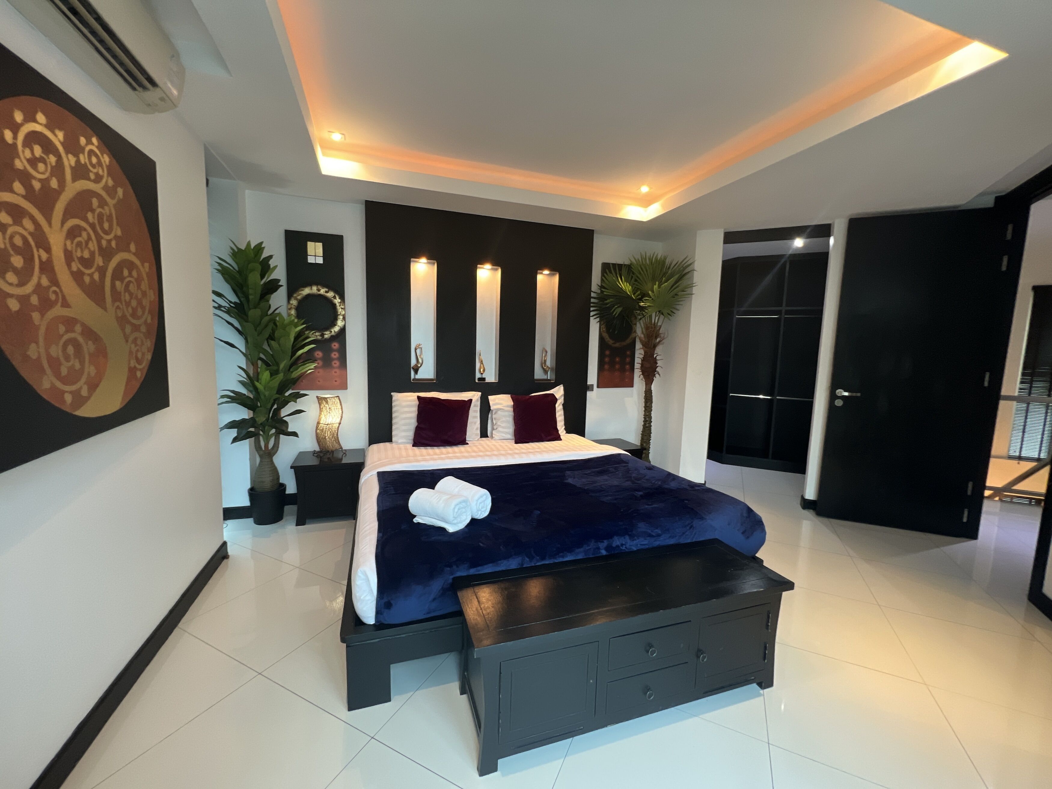 Un dormitorio moderno con una cama grande, mesitas de noche, un banco y una lámpara en el techo.