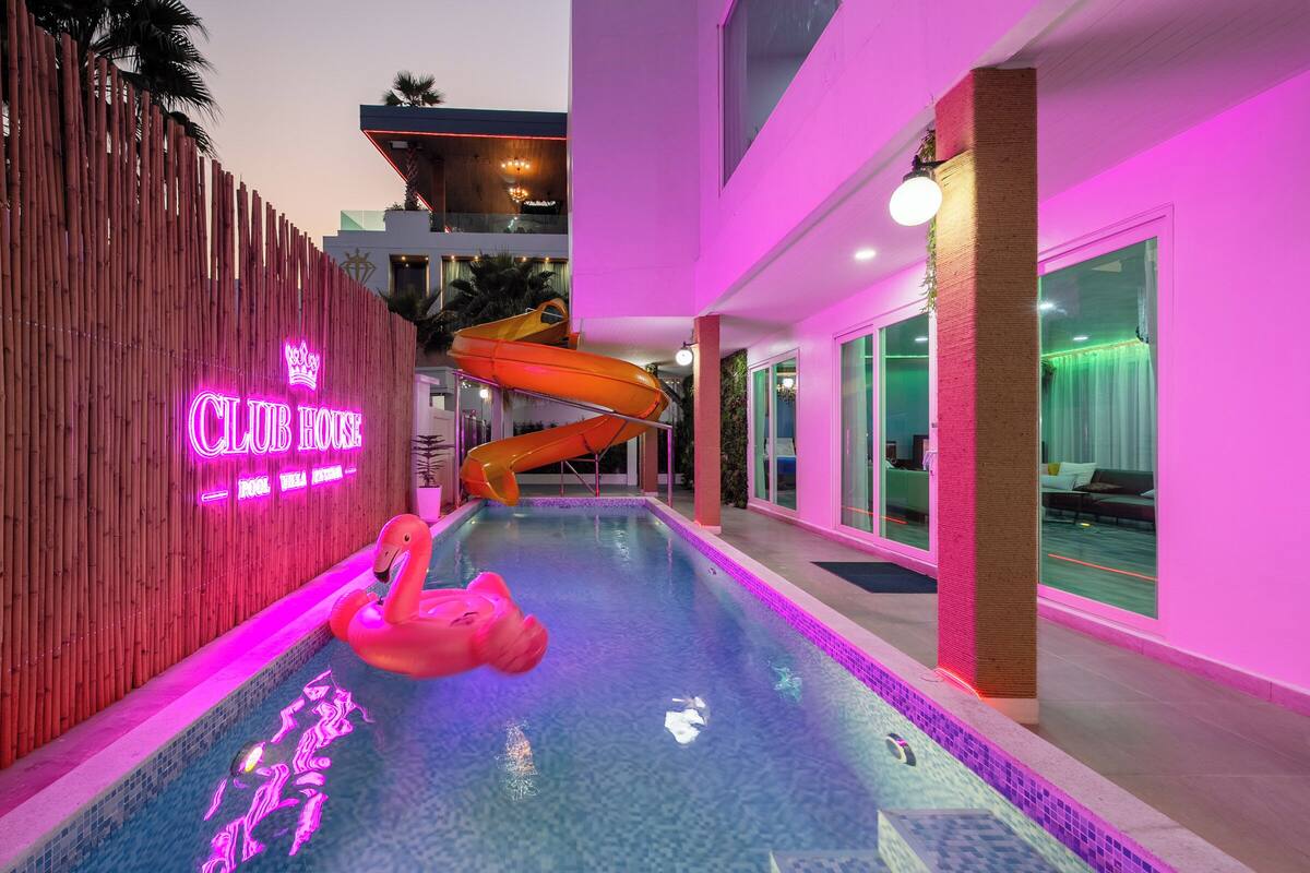 A swimming pool with a slide, a neon sign, and a pink flamingo float.