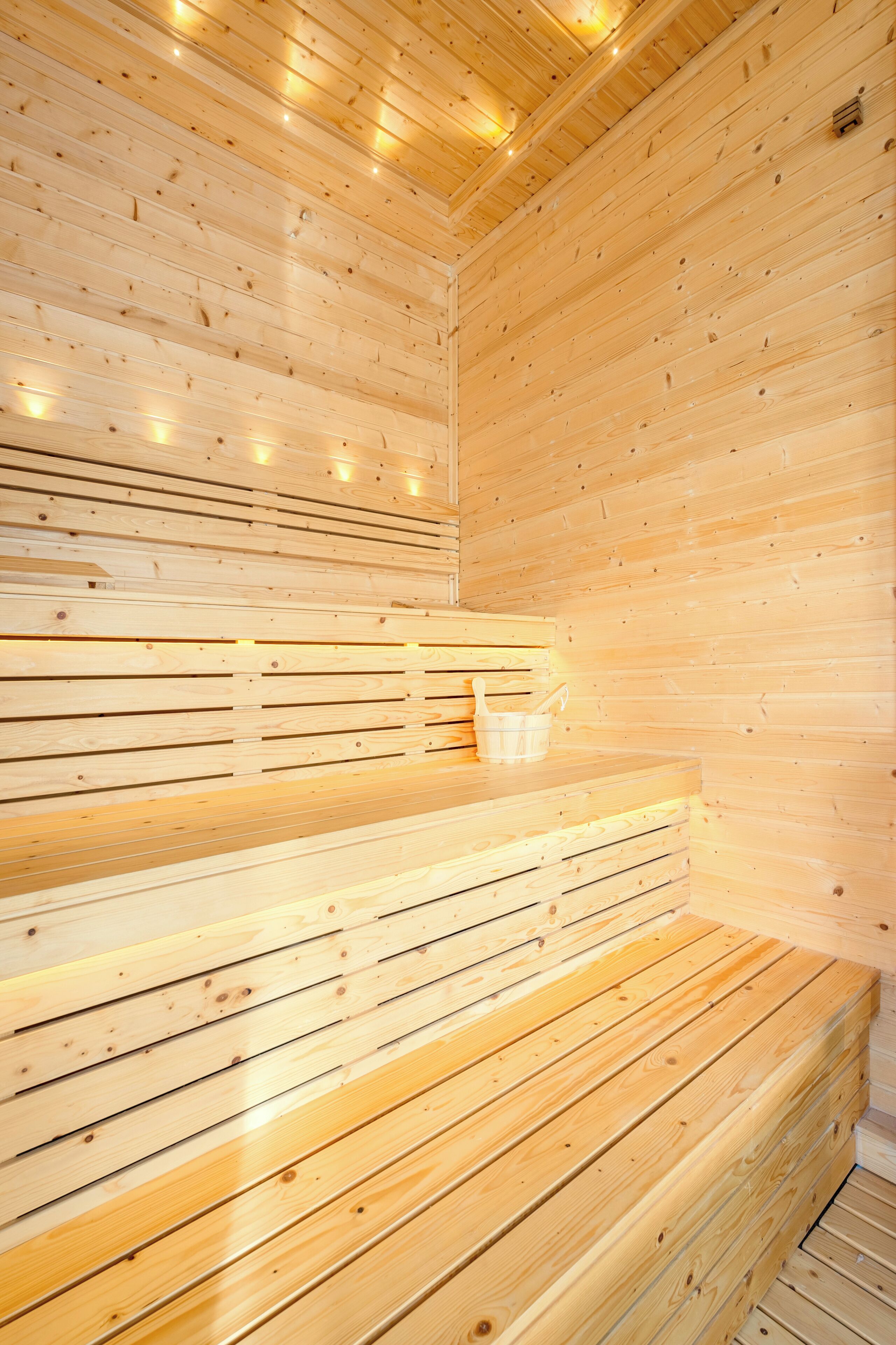 A wooden sauna with benches and a small bucket.