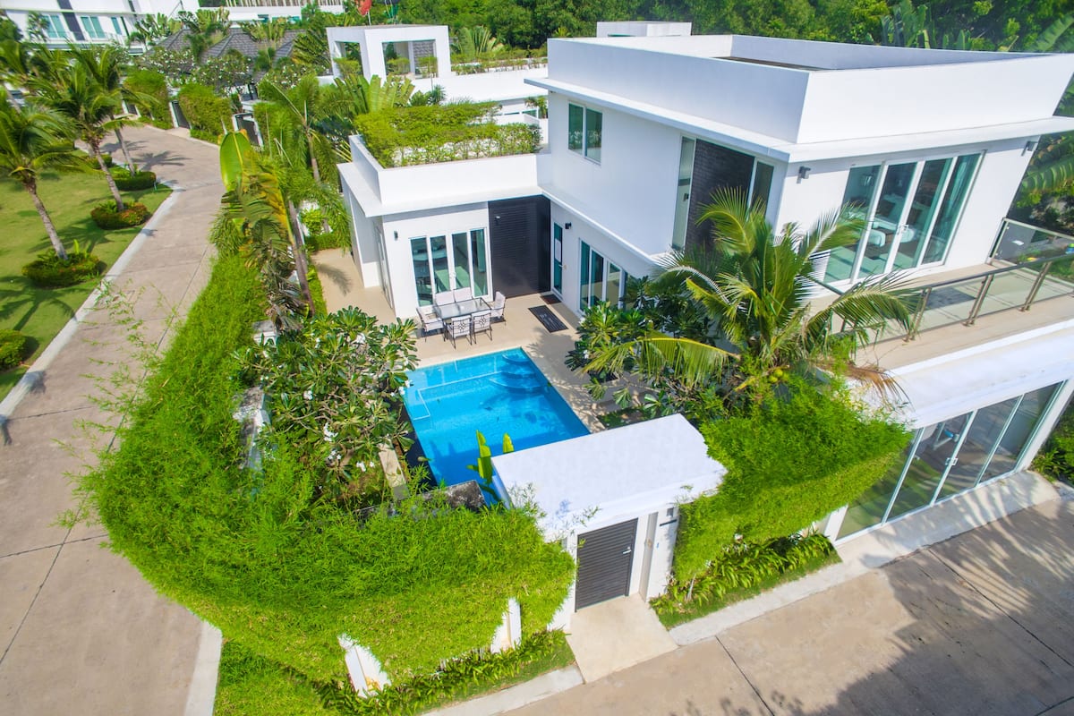A modern two-story house with a swimming pool surrounded by lush greenery.