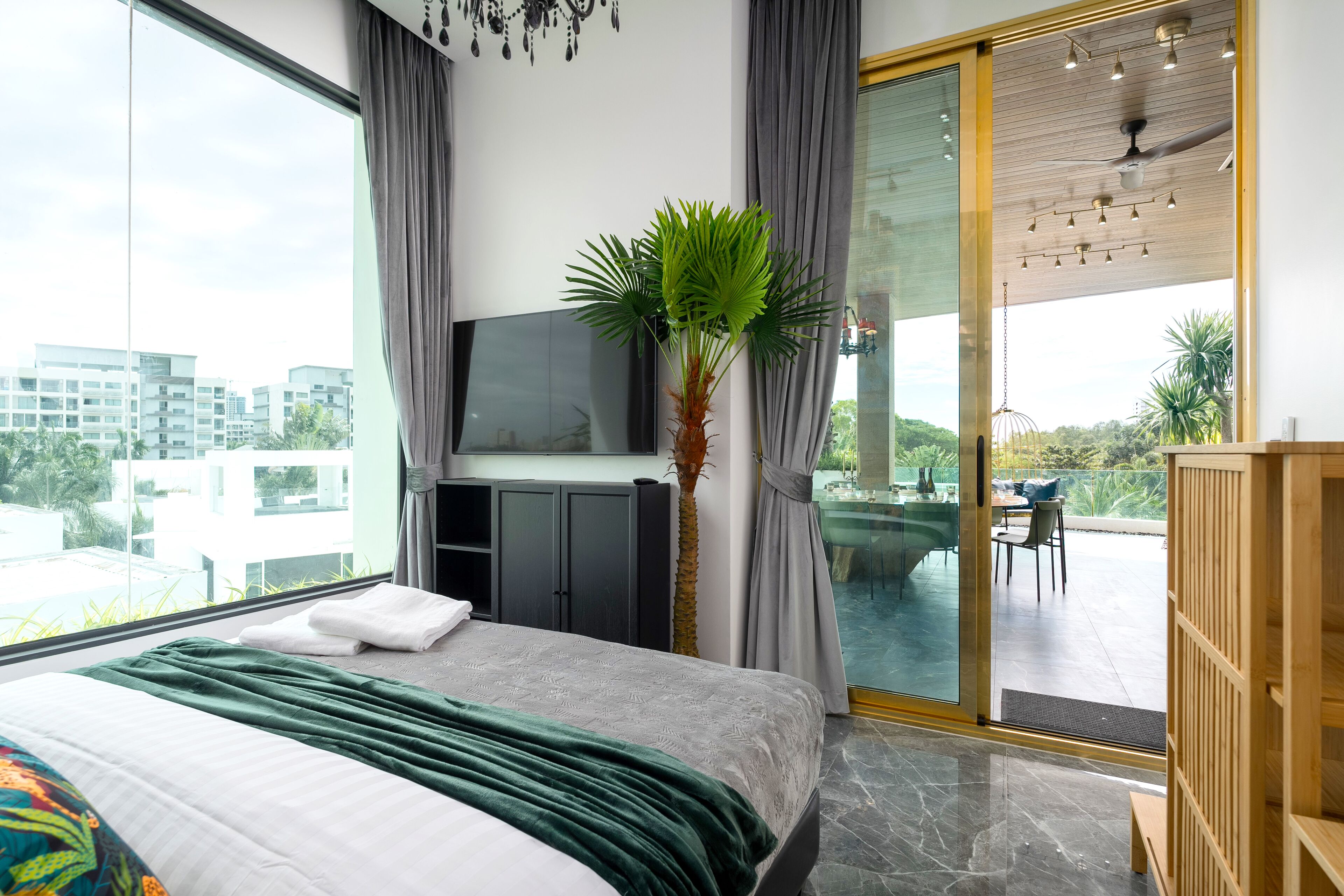 Ein modernes Hotelzimmer mit einem großen Bett, einem Fernseher, einer Pflanze und einem Balkon mit Blick auf die Stadt.