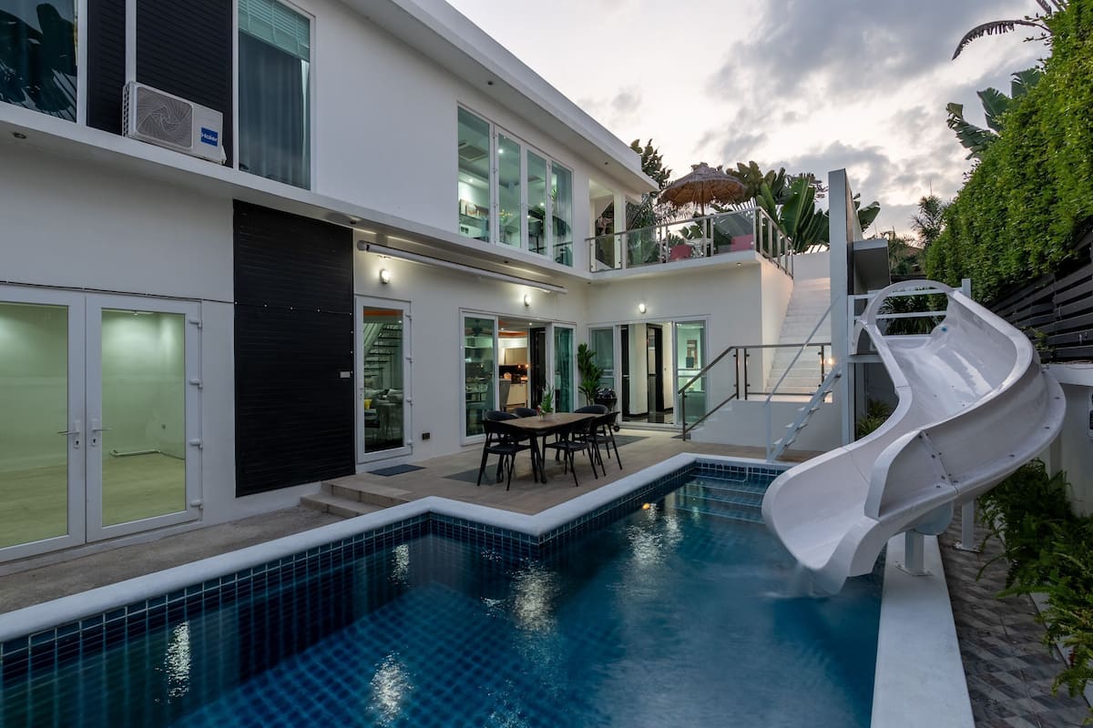 A modern house with a swimming pool, a slide, and a dining area.