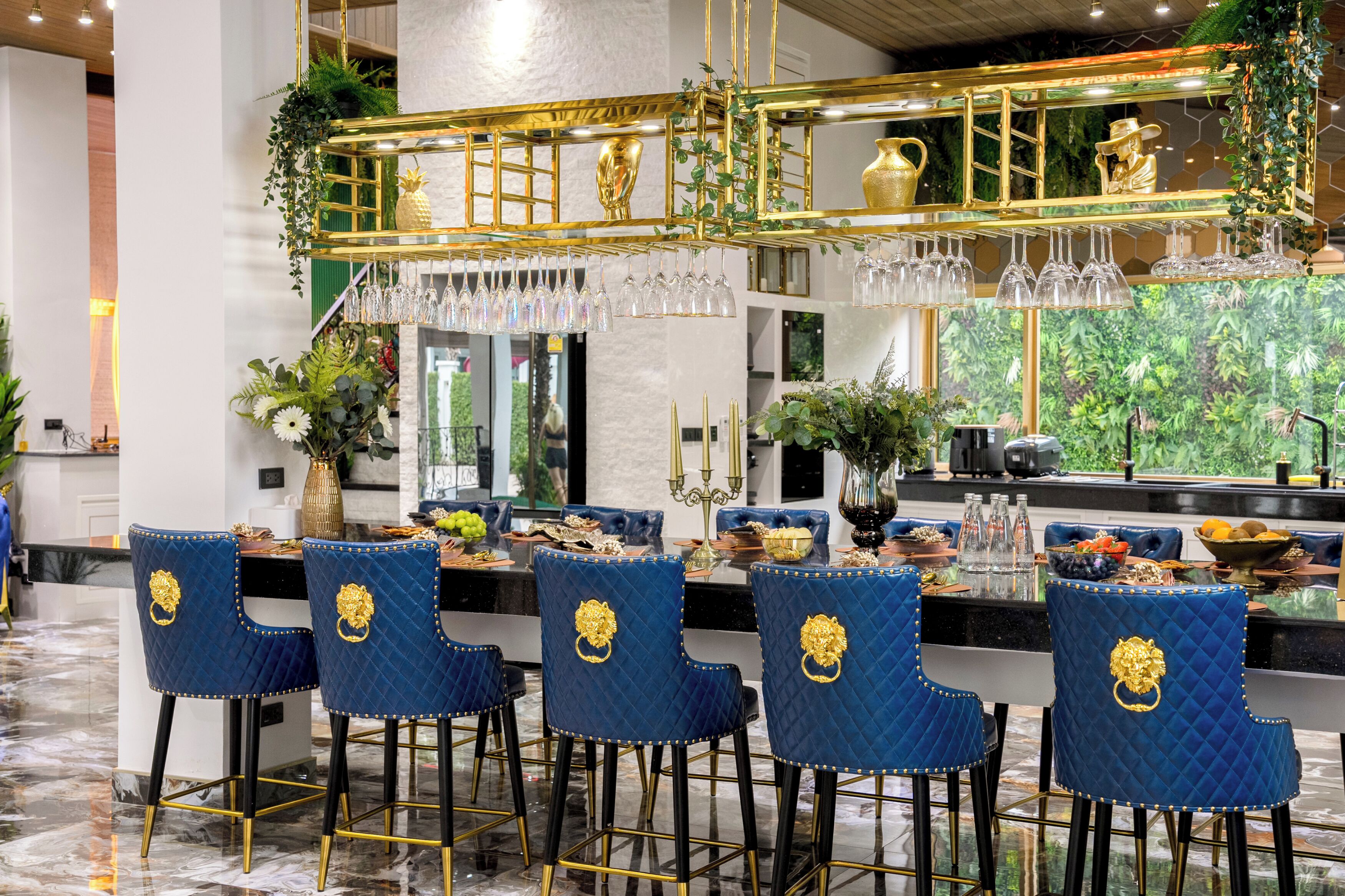 Eine Bar mit blauen Sitzmöglichkeiten, einer goldenen Theke und hängenden Weingläsern.