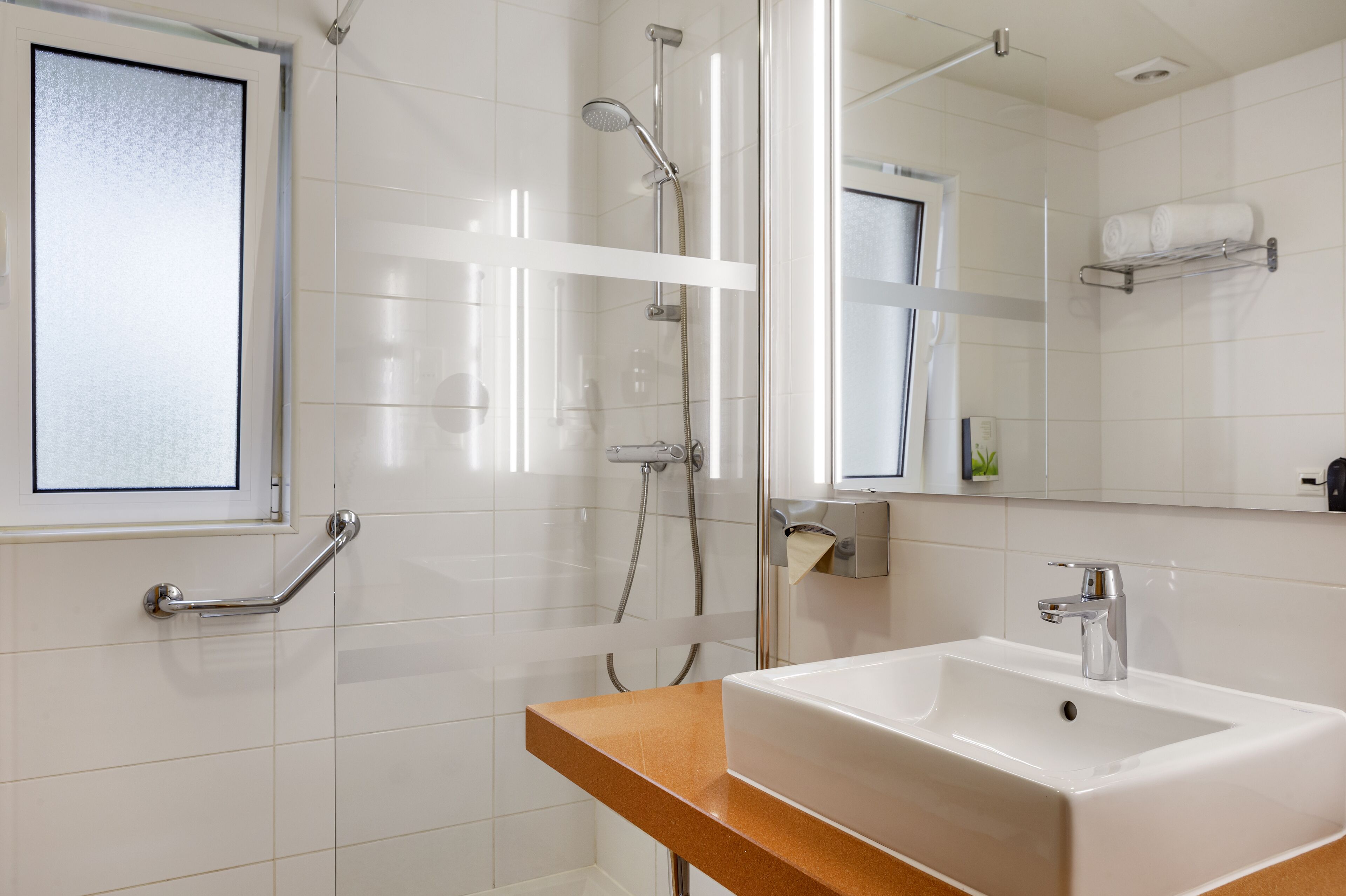A modern bathroom with a glass shower enclosure, a white sink, and a mirror with a towel rack above it.