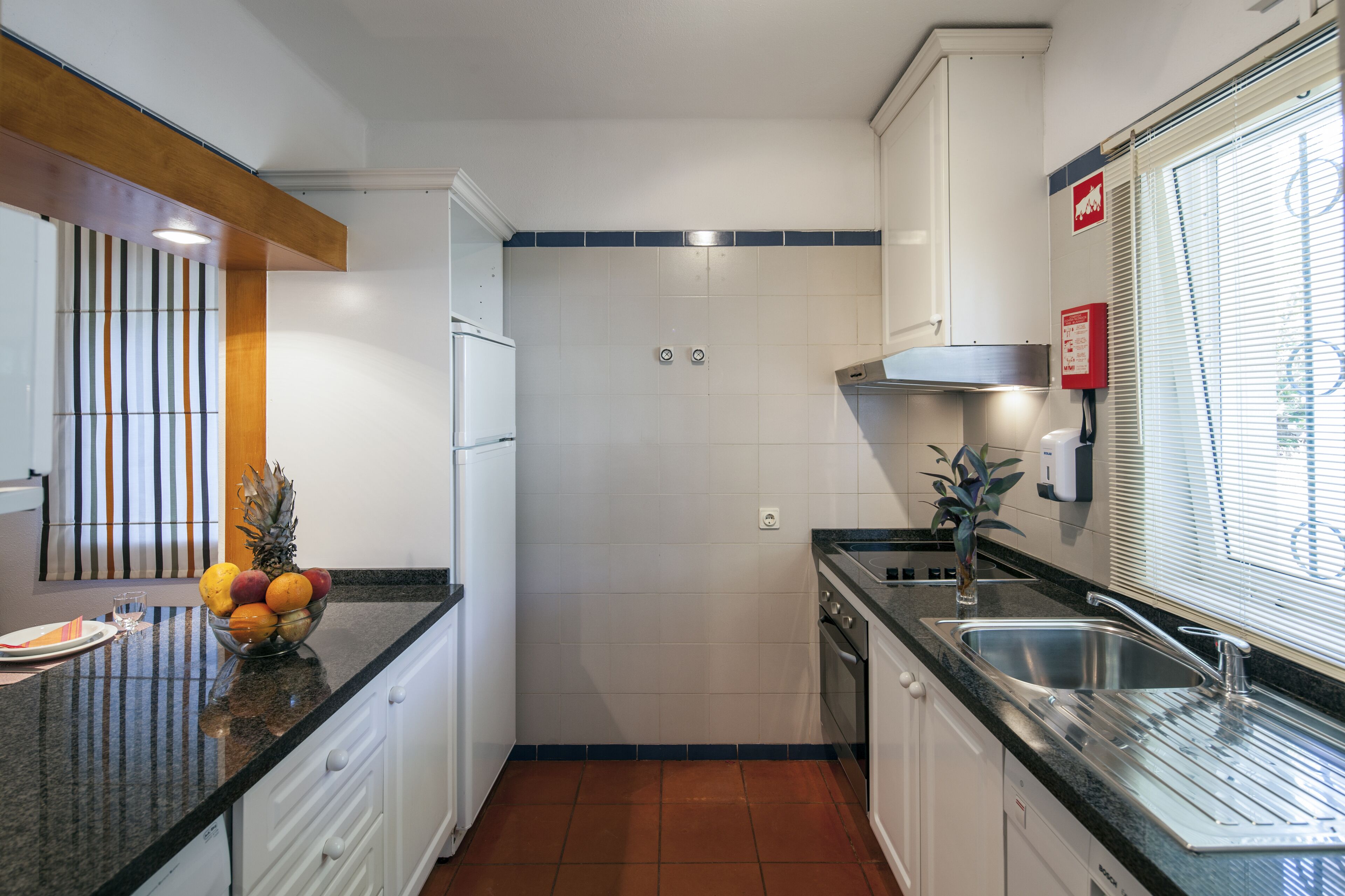 Una cucina compatta con mobili bianchi, un piano di lavoro nero e uno schienale piastrellato.