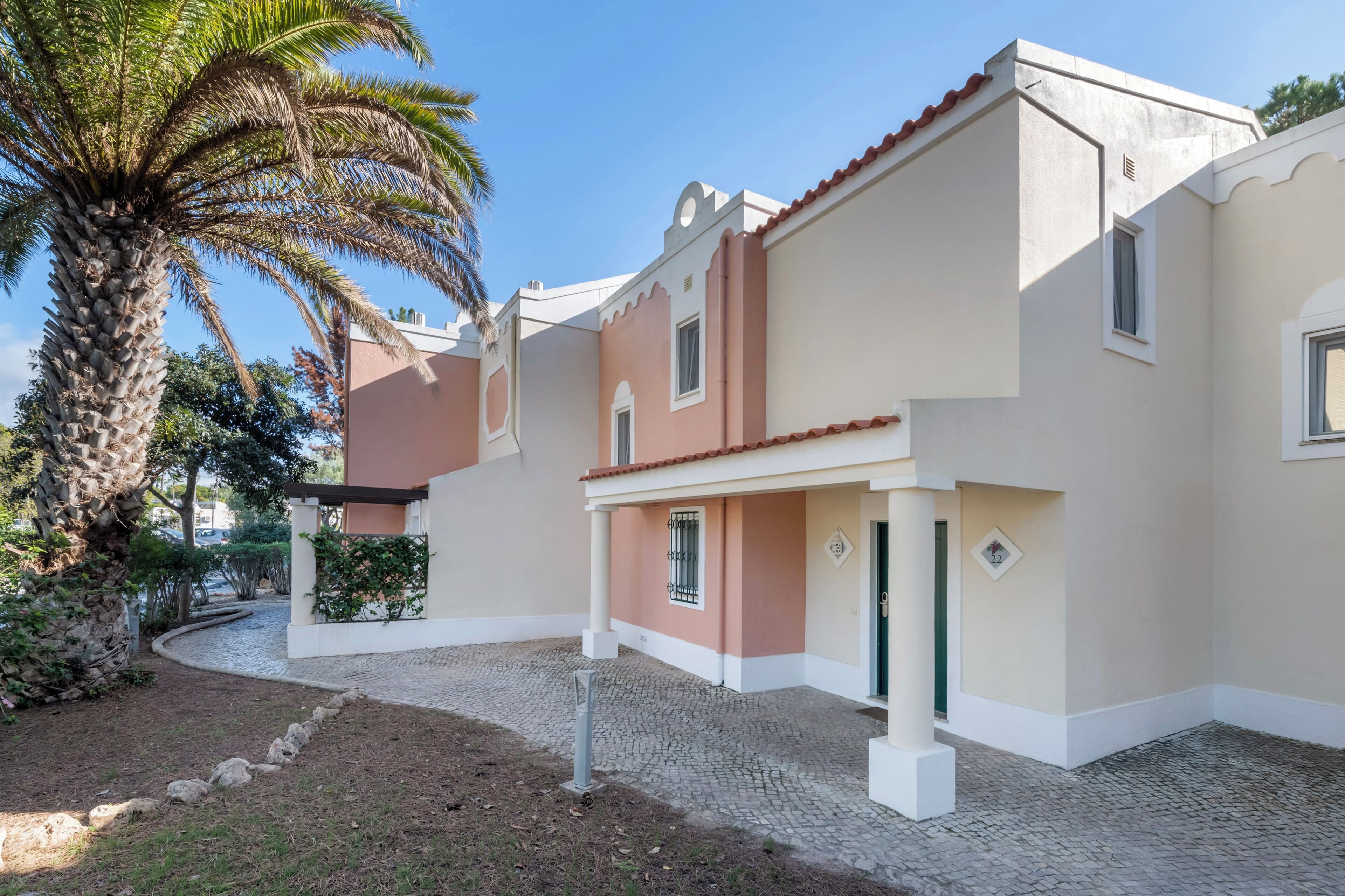 A building with a cobblestone entrance, a palm tree, and a small garden area.
