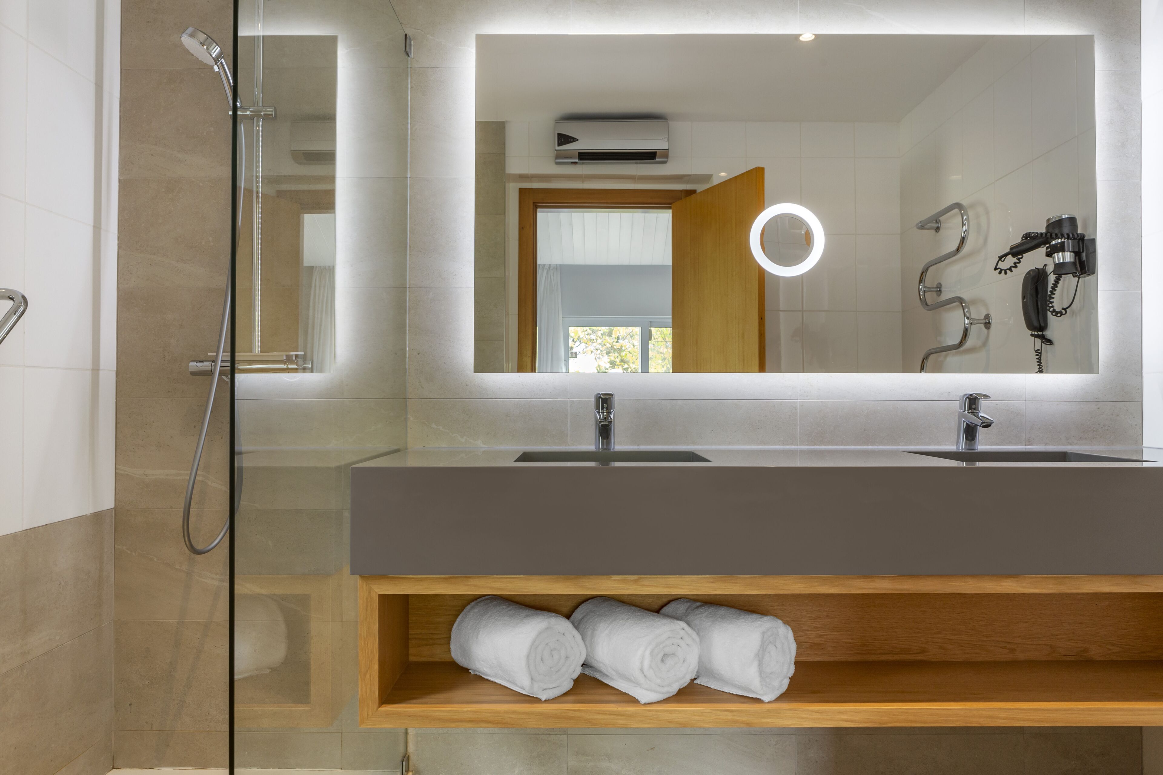 A modern bathroom with a large mirror, a shower, and a vanity with a towel shelf.