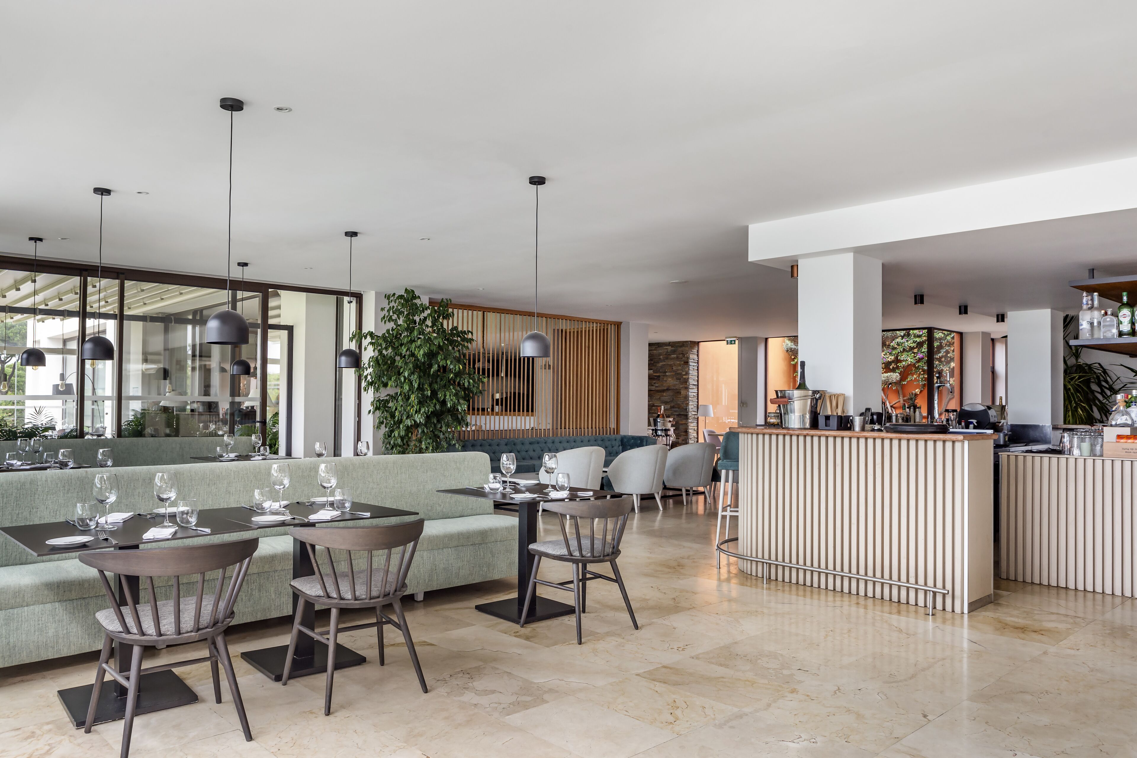 A modern restaurant with a green sofa, dining tables, and chairs. There is a bar area with a counter and stools.