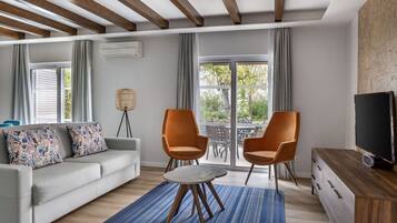 A modern living room with a sofa, two armchairs, a coffee table, a TV, and a large window with a view of greenery.