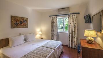 A bedroom with a bed, two bedside tables, a lamp, a mirror, and a window with curtains.