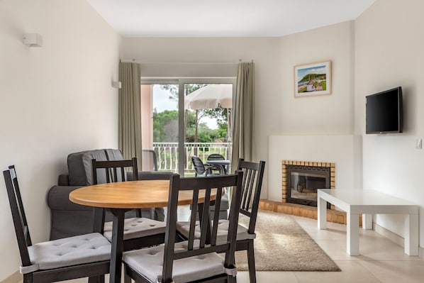 A modern living room with a dining area, a fireplace, and a TV. - Vilar Do Golf (Loulé)