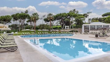 A swimming pool with lounge chairs and umbrellas, surrounded by trees and a clear sky.