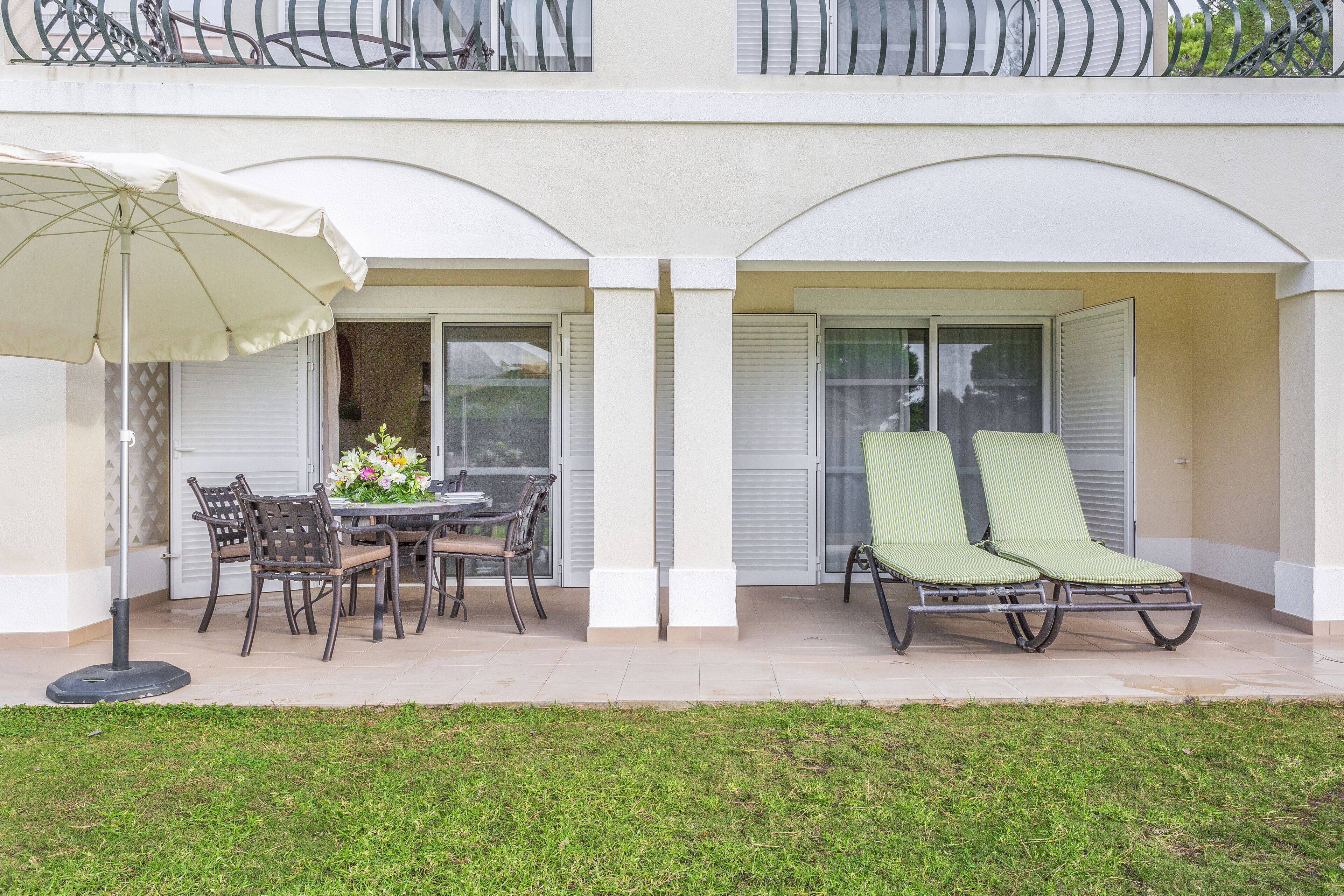 Un patio al aire libre con una mesa, sillas, una sombrilla y dos sillones.