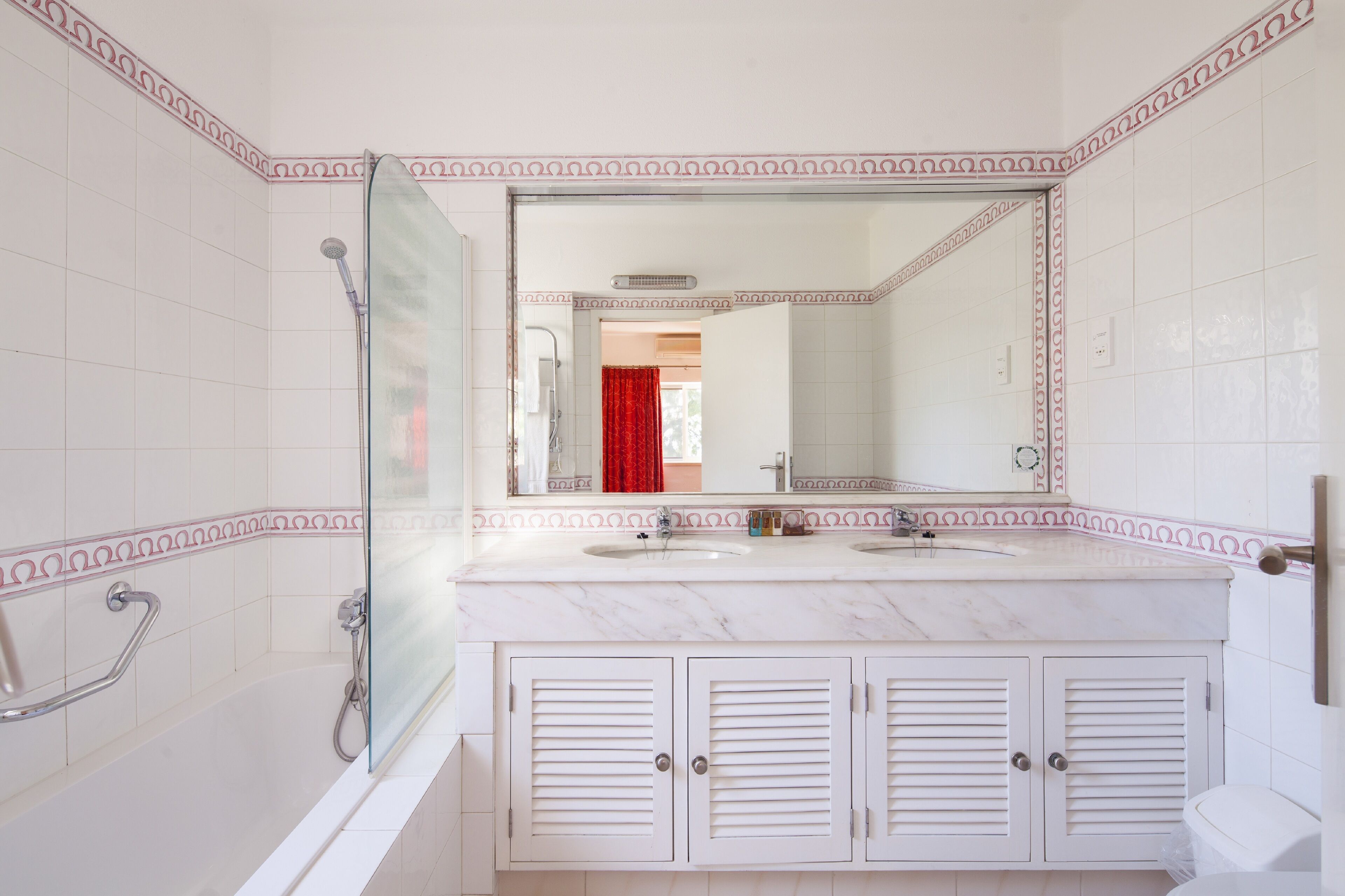 Een badkamer met een witte betegelde muur, een grote spiegel, een badkuip en een wastafelmeubel met kastjes.