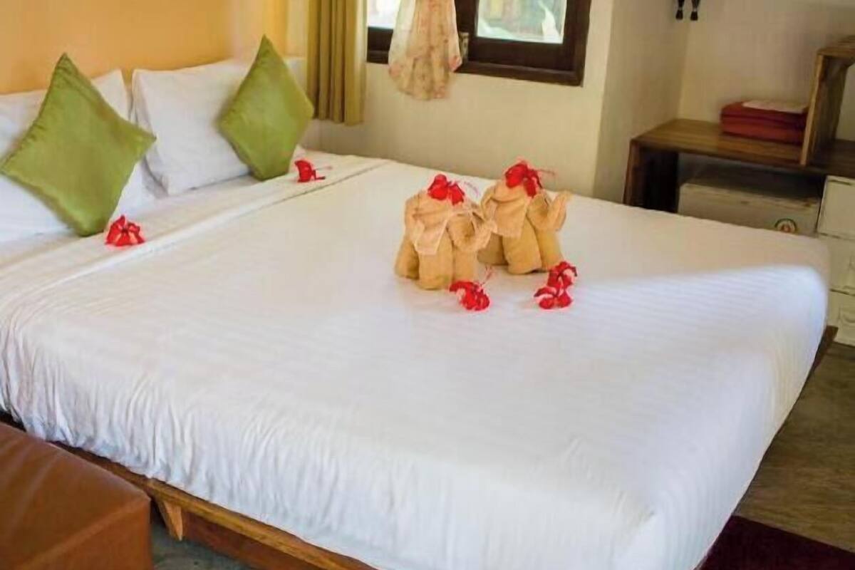 Una cama bien hecha con sábanas blancas, almohadas verdes y un pequeño objeto rojo sobre la cama.