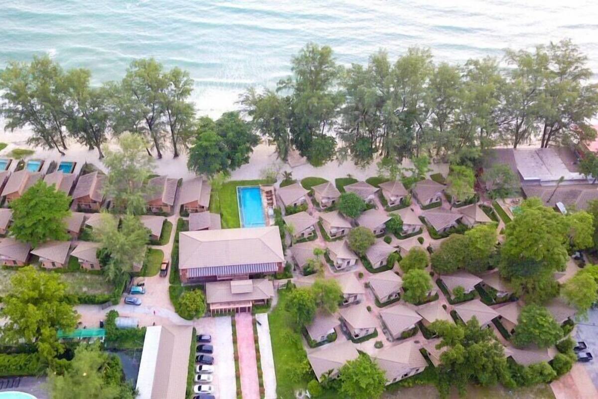 Vista aérea de un complejo turístico con varias cabañas y una piscina central frente a la playa.