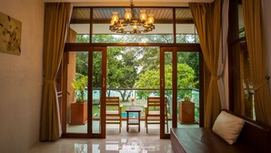 Habitación con un amplio ventanal corredera que da a un espacio exterior con piscina y vegetación. Un candelabro cuelga del techo, y un sofá con cojines se encuentra cerca de la puerta.