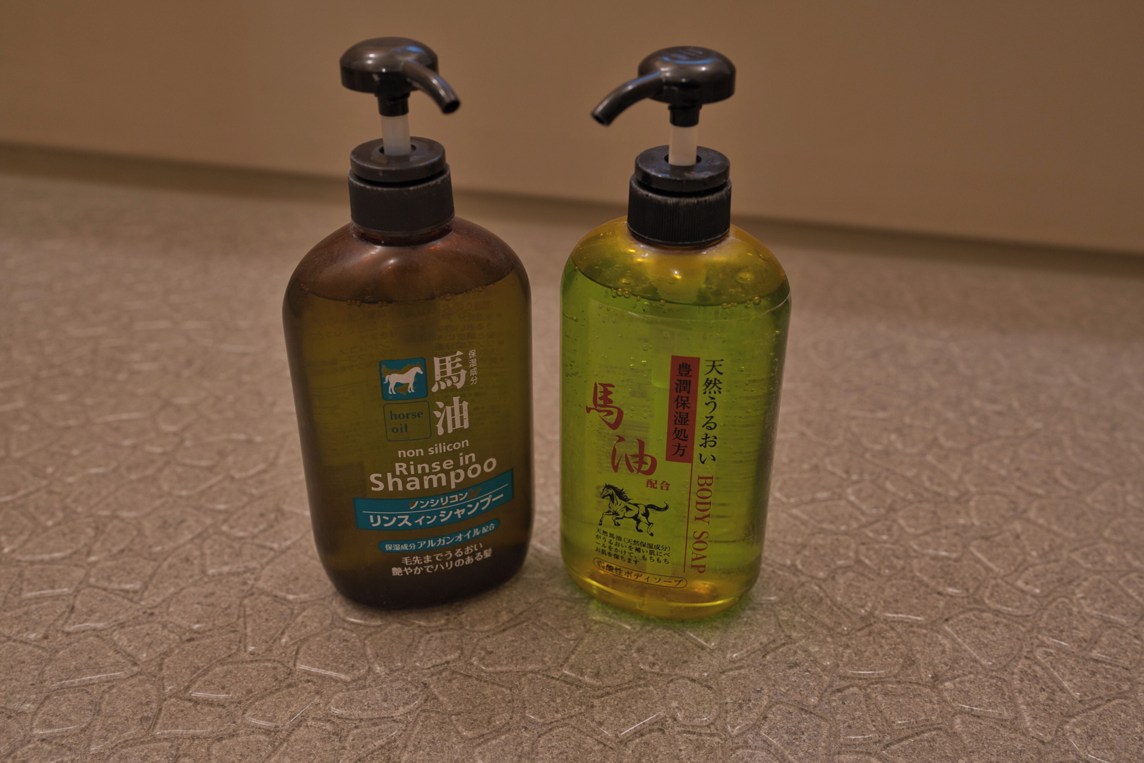 Two bottles of shampoo with pump dispensers on a textured surface.