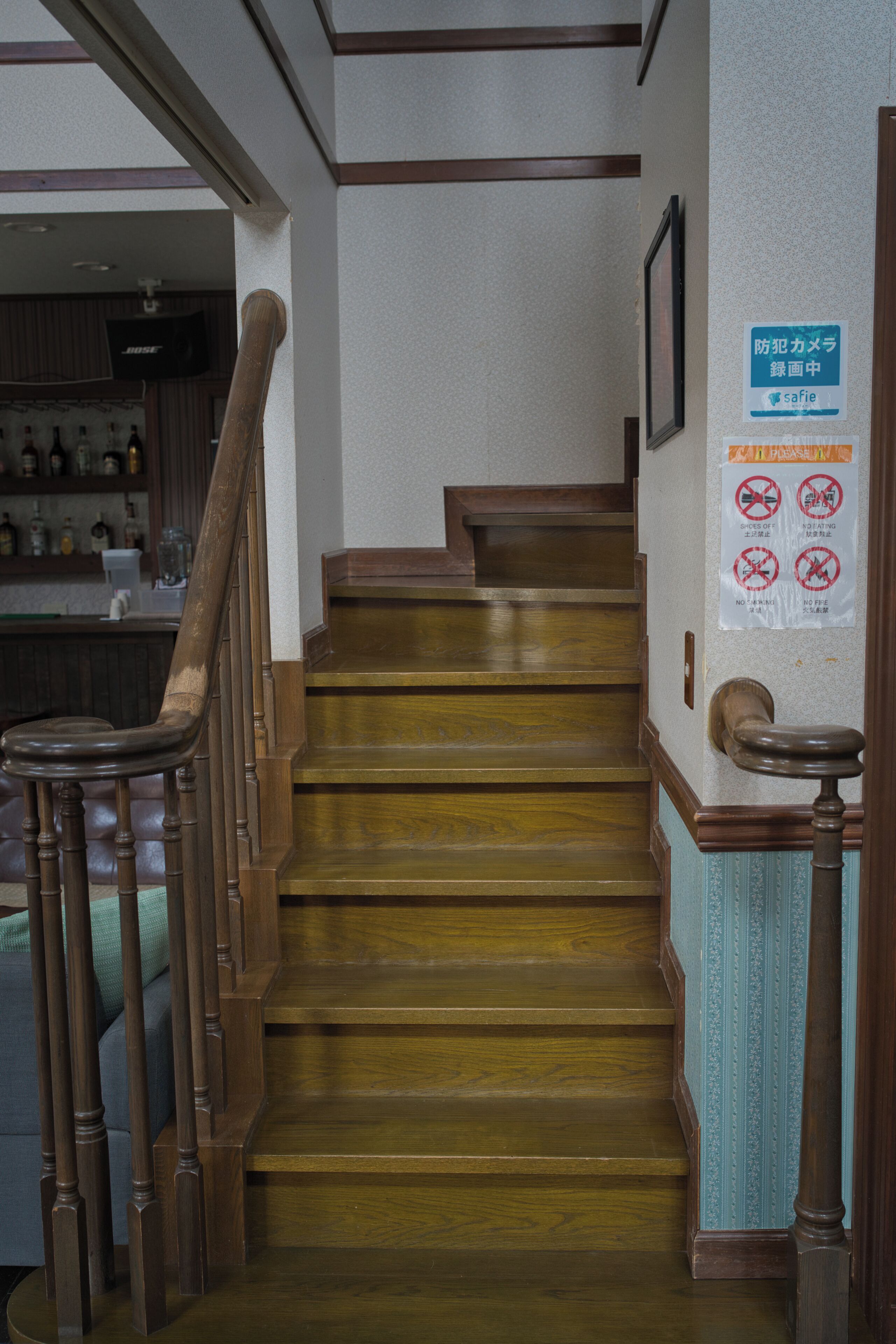 Un escalier en bois avec une rampe, un mur orné de panneaux de signalisation de sécurité et, au fond, un espace bar.