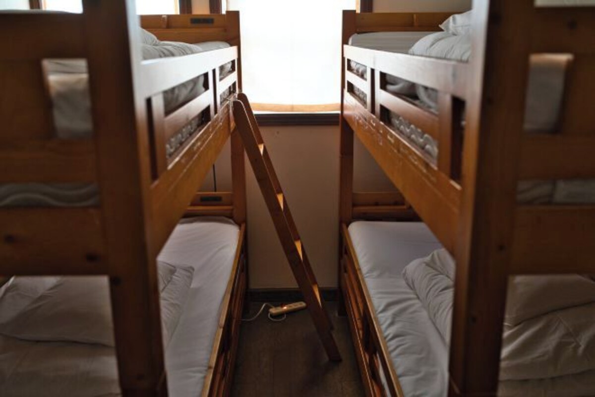 Une chambre avec un lit superposé, dont la structure est en bois et dont la literie est blanche.