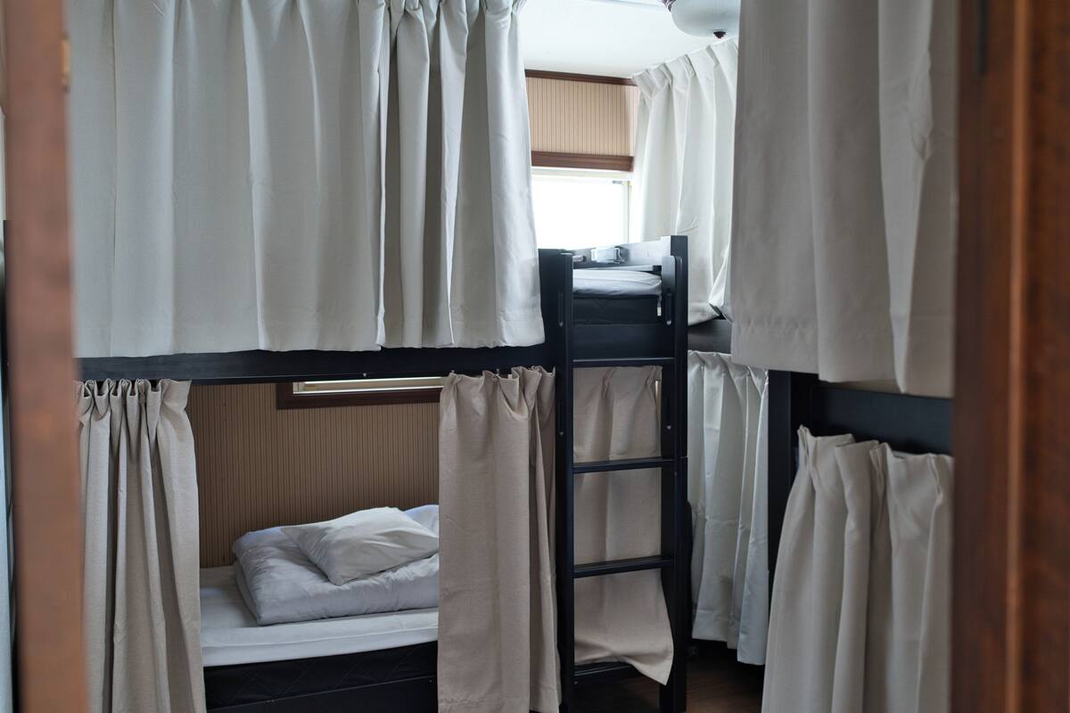 Dormitorio con literas, cortinas, una escalera y ventana con persianas.