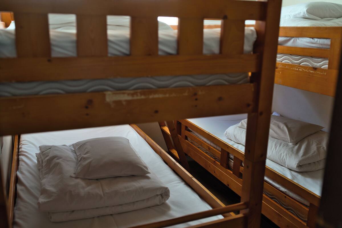 Una cama individual con cabecera y barandillas de madera, ropa de cama blanca y vistas al cielo entre las listones.