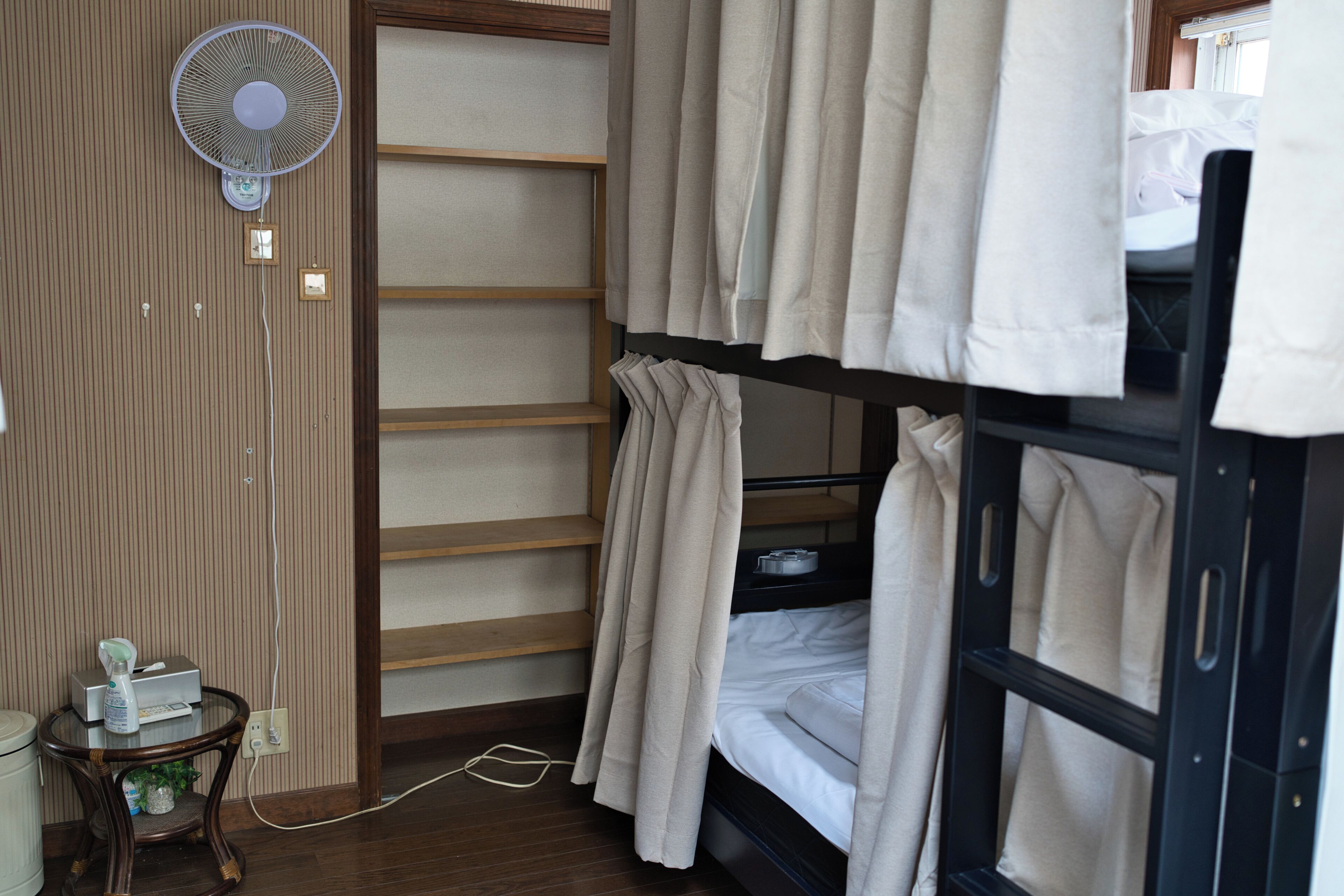 A bunk bed room with a fan, a small table with a plant, and a window with curtains.