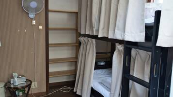 A bunk bed room with a fan, a small table with a plant, and a window with curtains.